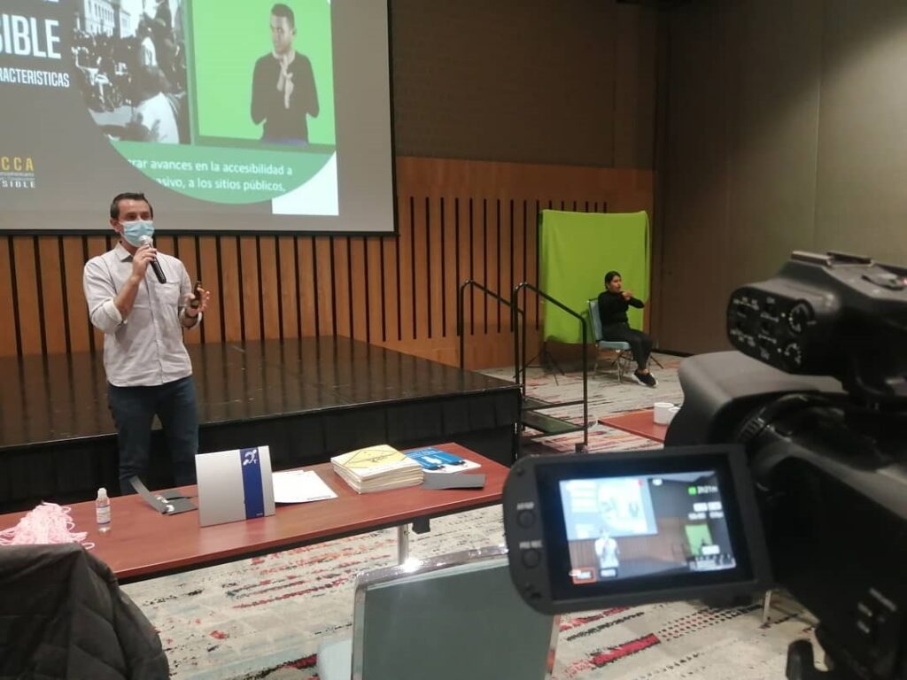Imagen de conferencia en auditorio, ponente e interprete de lengua de señas 